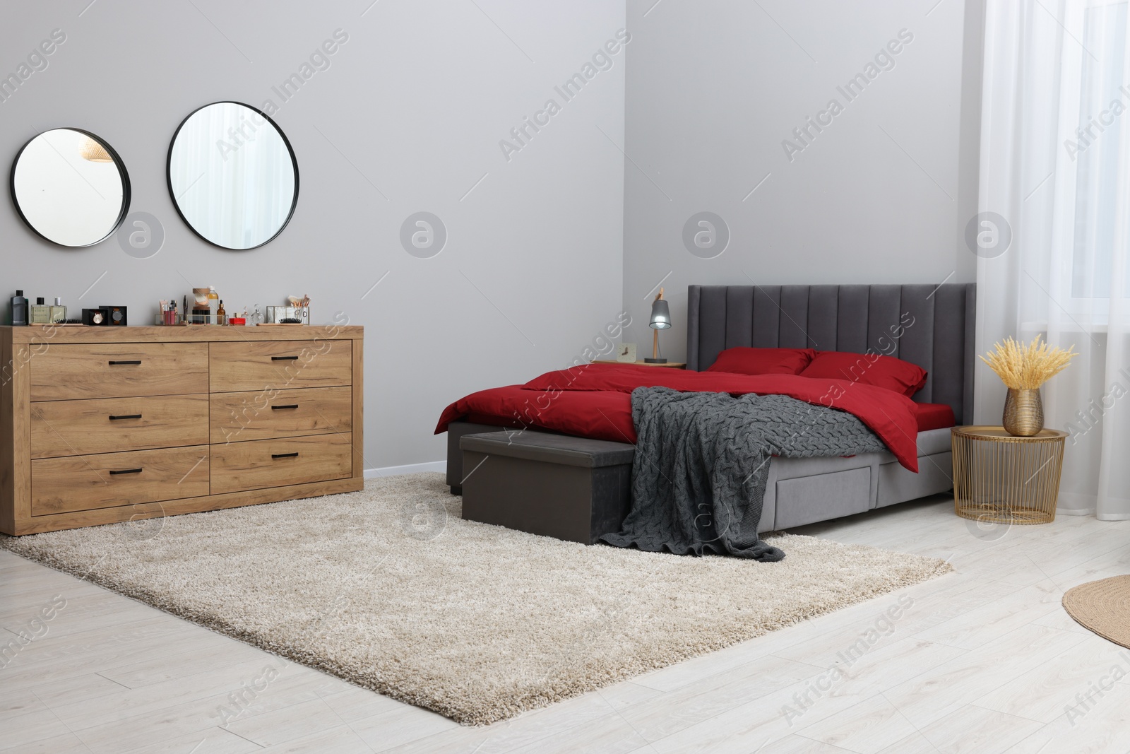 Photo of Stylish bedroom with comfortable bed and wooden chest of drawers. Interior design