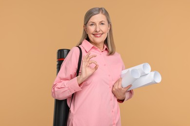 Photo of Architect with drafts and tube showing ok gesture on beige background