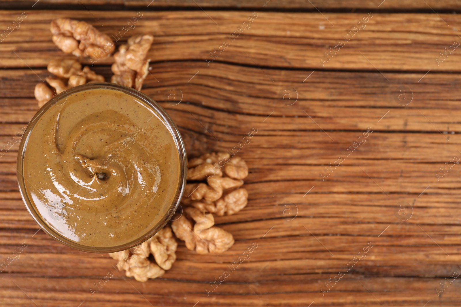 Photo of Delicious nut butter in bowl and walnuts on wooden table, top view. Space for text