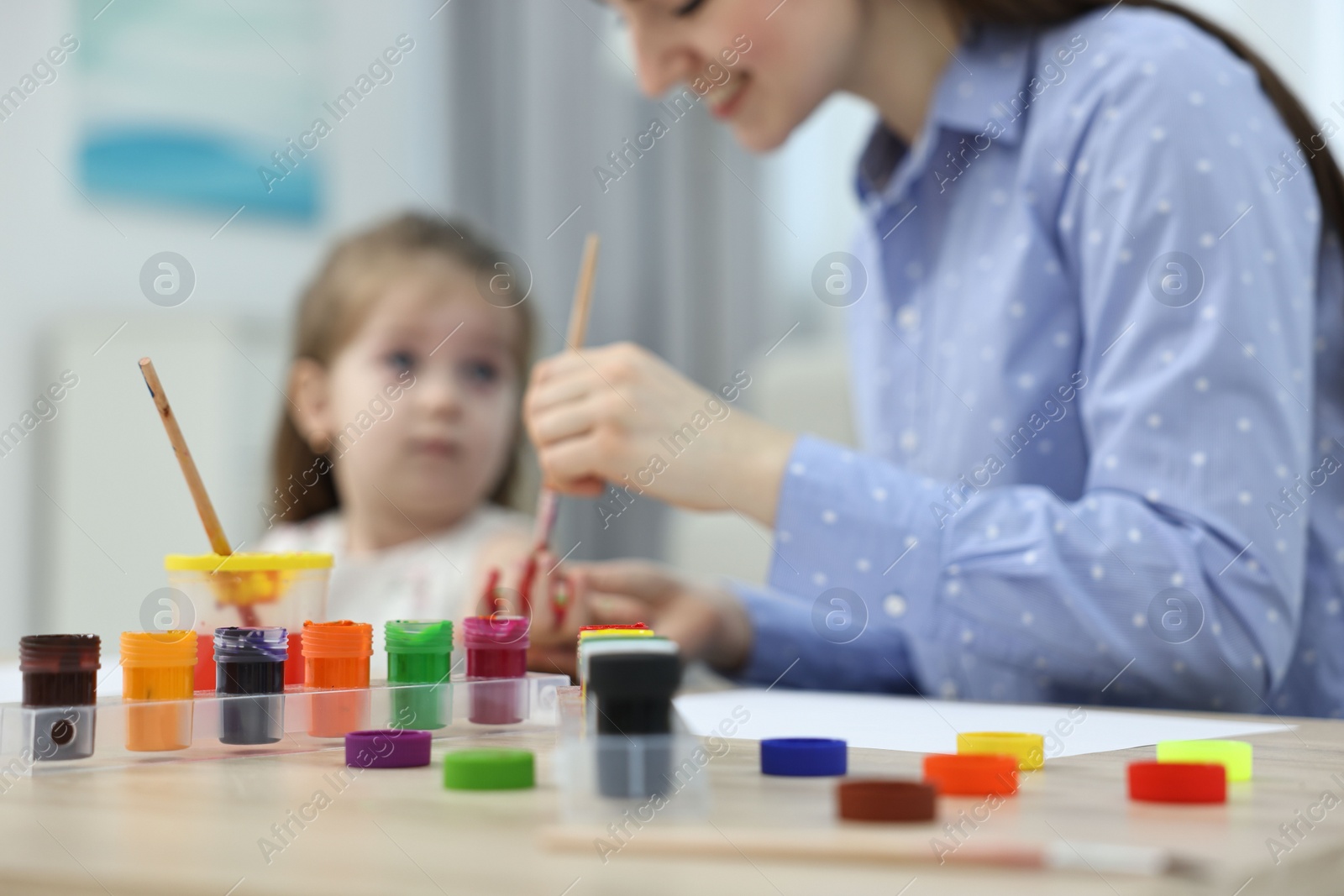 Photo of Mother and her little daughter painting with palms at home, selective focus