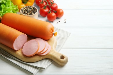 Photo of Board with tasty boiled sausages and products on white wooden table. Space for text