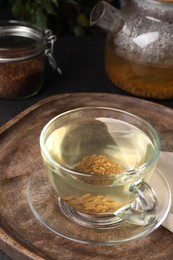 Photo of Buckwheat tea in glass cup on wooden tray, closeup