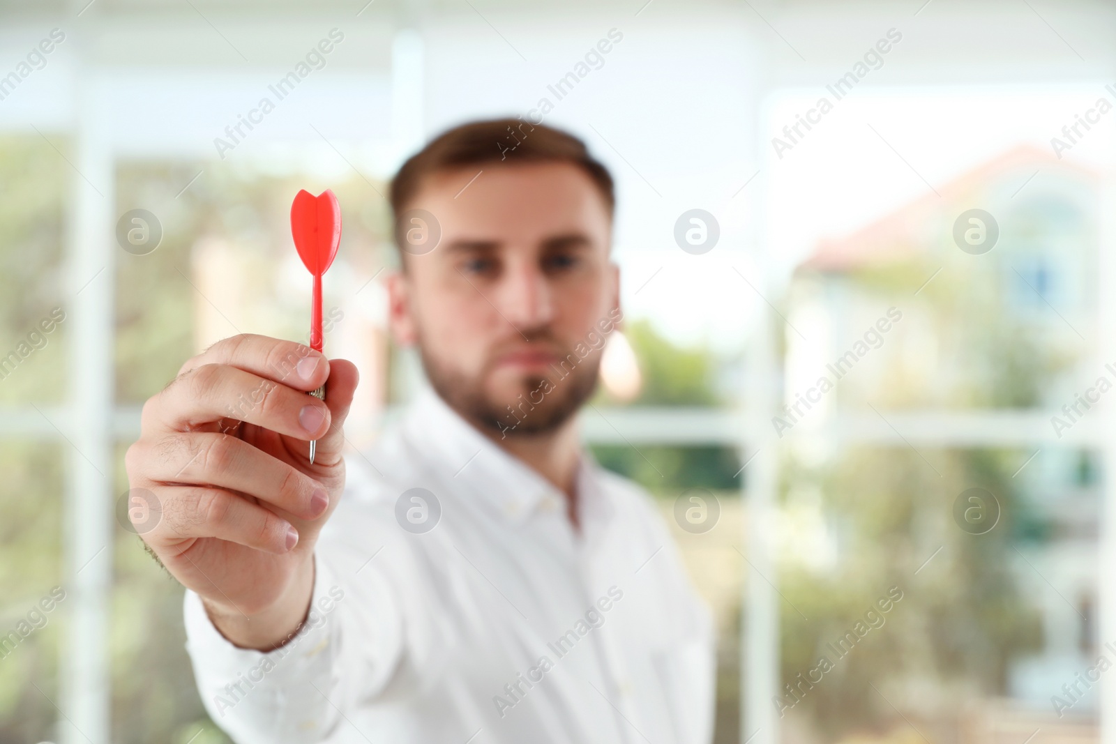Photo of Young businessman indoors, focus on hand with dart
