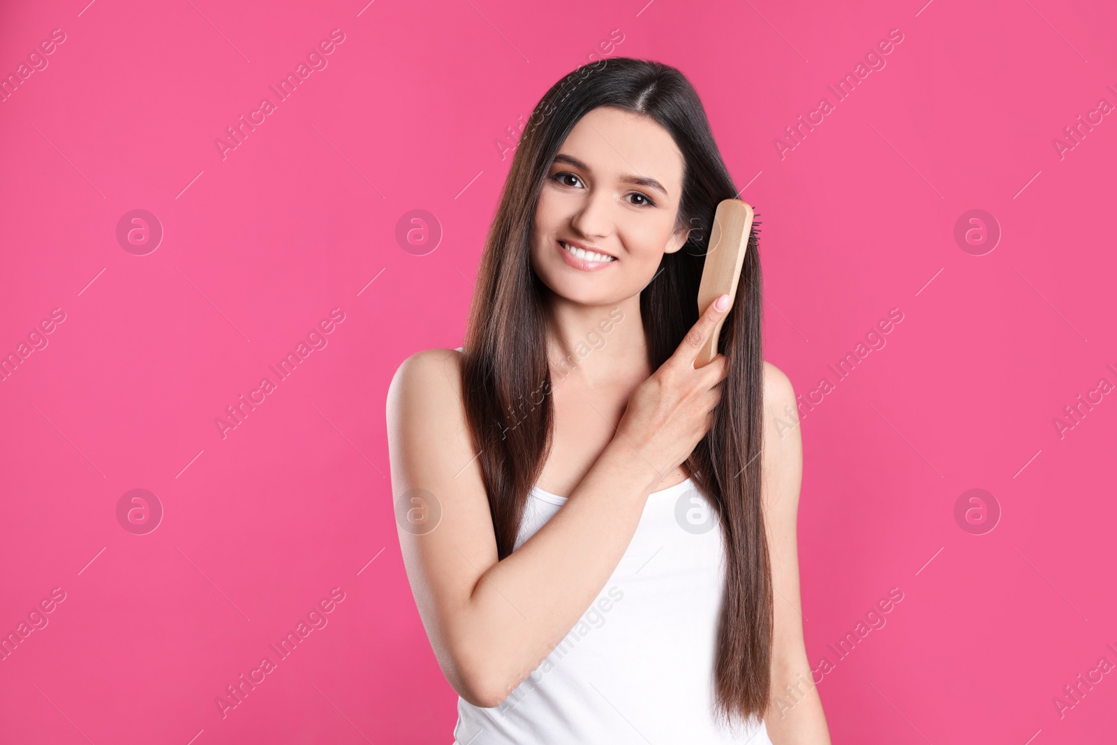 Photo of Beautiful smiling young woman with hair brush on color background