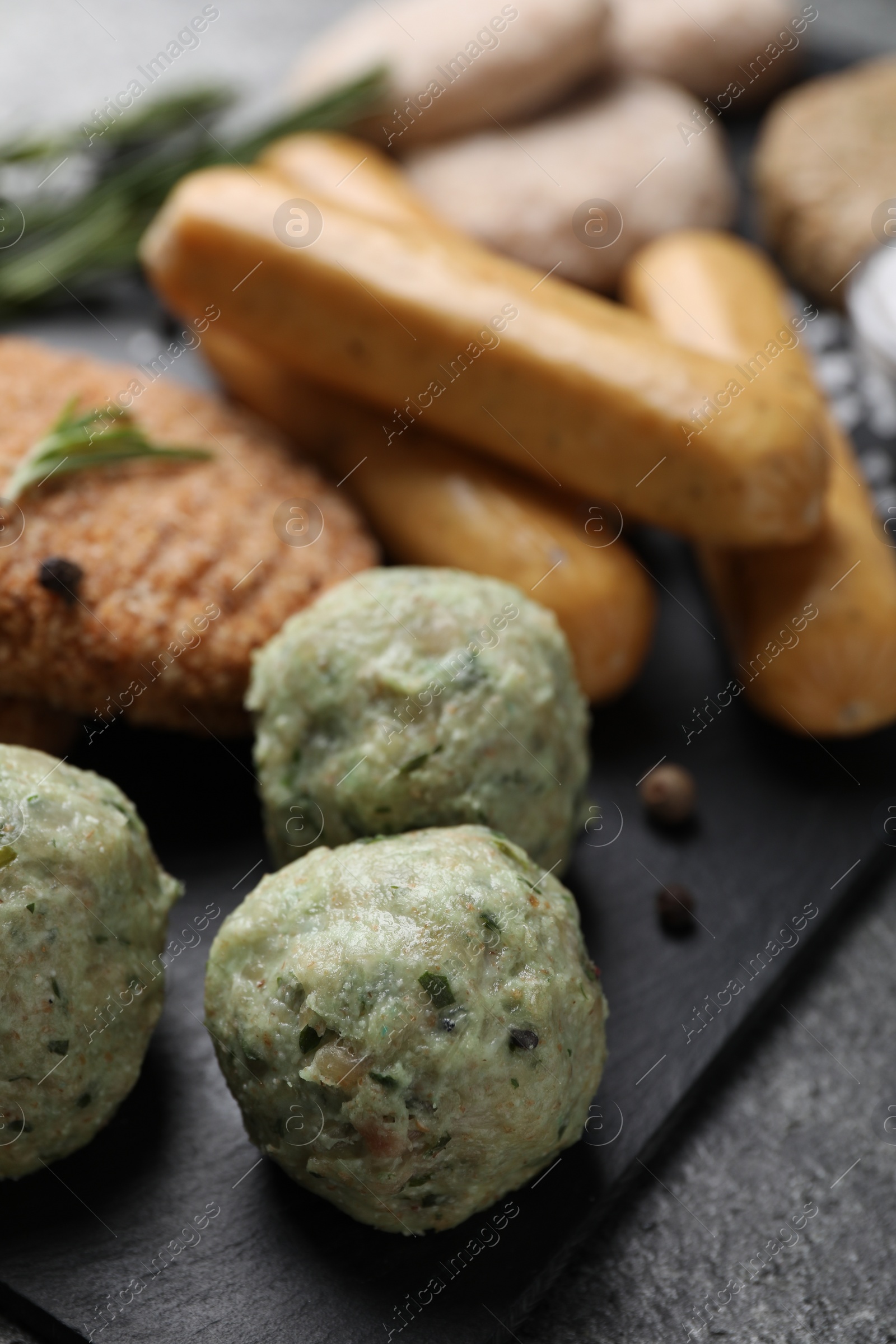 Photo of Falafel balls and different raw vegan meat products on dark board, closeup