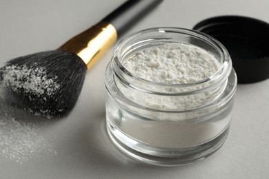 Photo of Rice loose face powder and makeup brush on light grey background, closeup