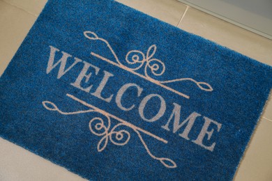 Photo of Beautiful blue doormat with word Welcome on floor near entrance, above view