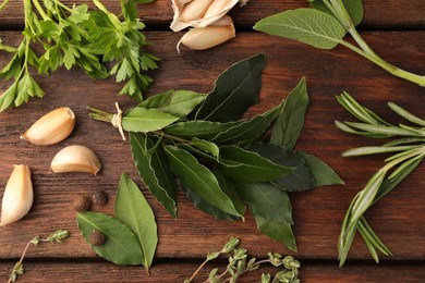 Aromatic bay leaves, different herbs and spices on wooden table, flat lay