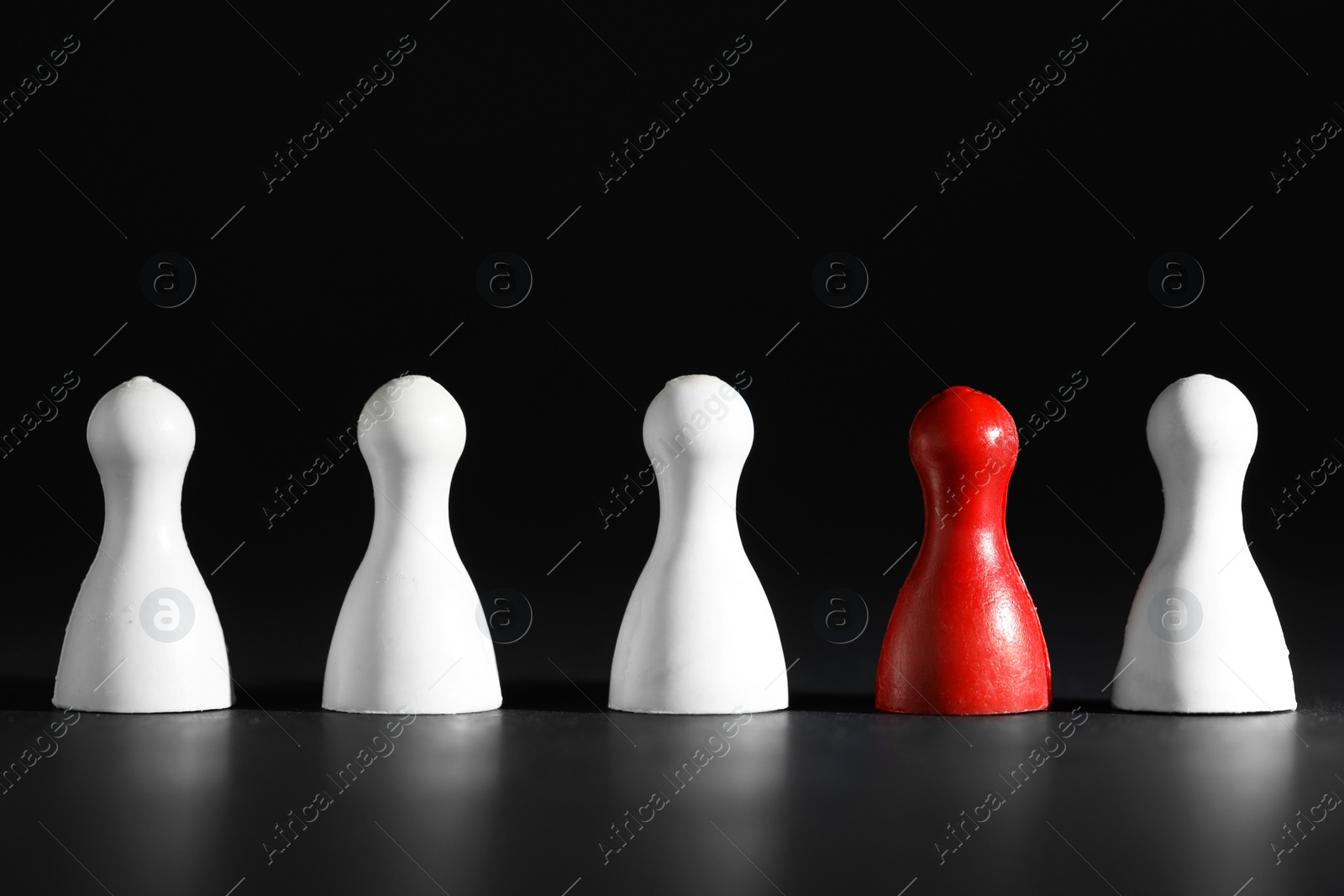 Photo of Choice concept. Red pawn among white ones on black table, closeup