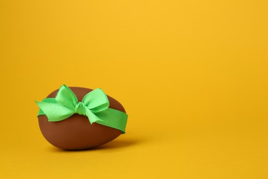 Photo of One tasty chocolate egg with green ribbon on orange background. Space for text