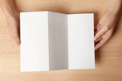 Woman holding blank brochure mock up on wooden table, top view