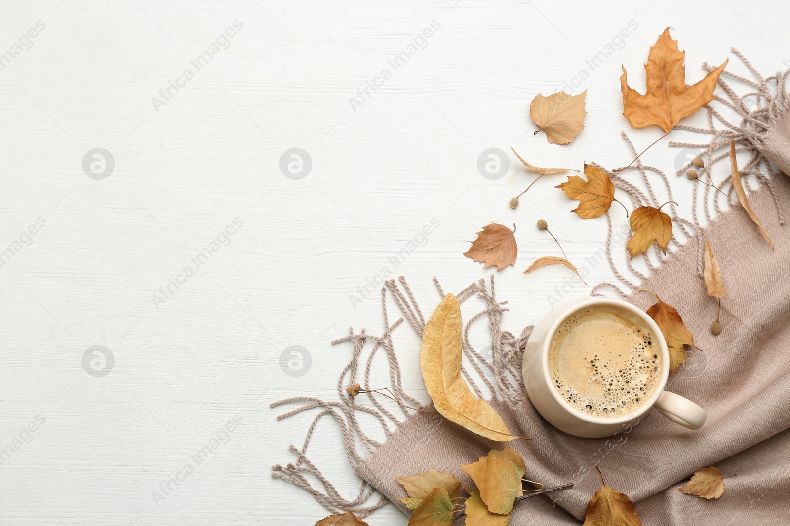 Photo of Flat lay composition with cup of hot drink and autumn leaves on white wooden table, space for text. Cozy atmosphere