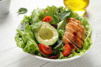Photo of Delicious salad with chicken, cherry tomato and avocado on white wooden table, closeup