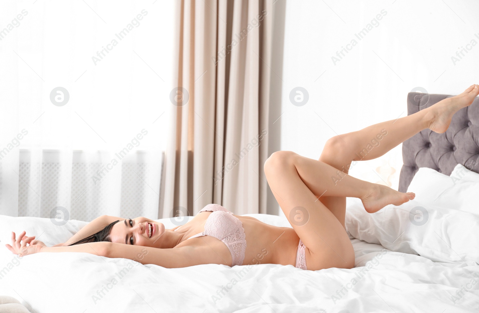 Photo of Beautiful young woman in pink underwear lying on bed at home