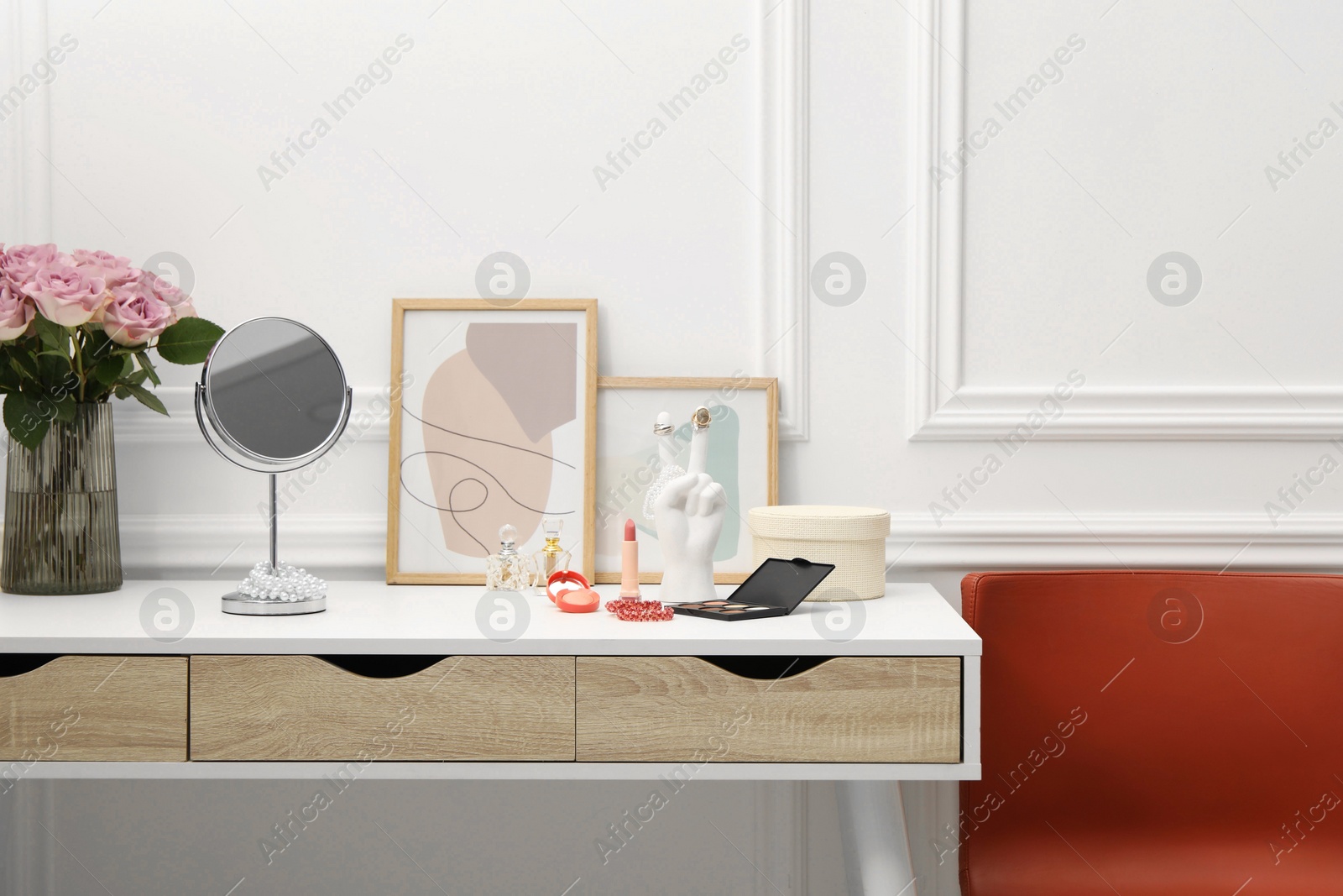 Photo of Mirror, cosmetic products, perfumes and vase with pink roses on white dressing table in makeup room