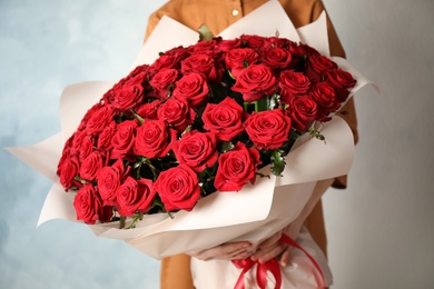 Photo of Woman holding luxury bouquet of fresh red roses on light background, closeup