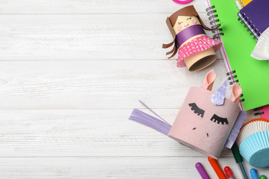 Photo of Doll and unicorn made of toilet paper among stationery on white wooden table, flat lay. Space for text