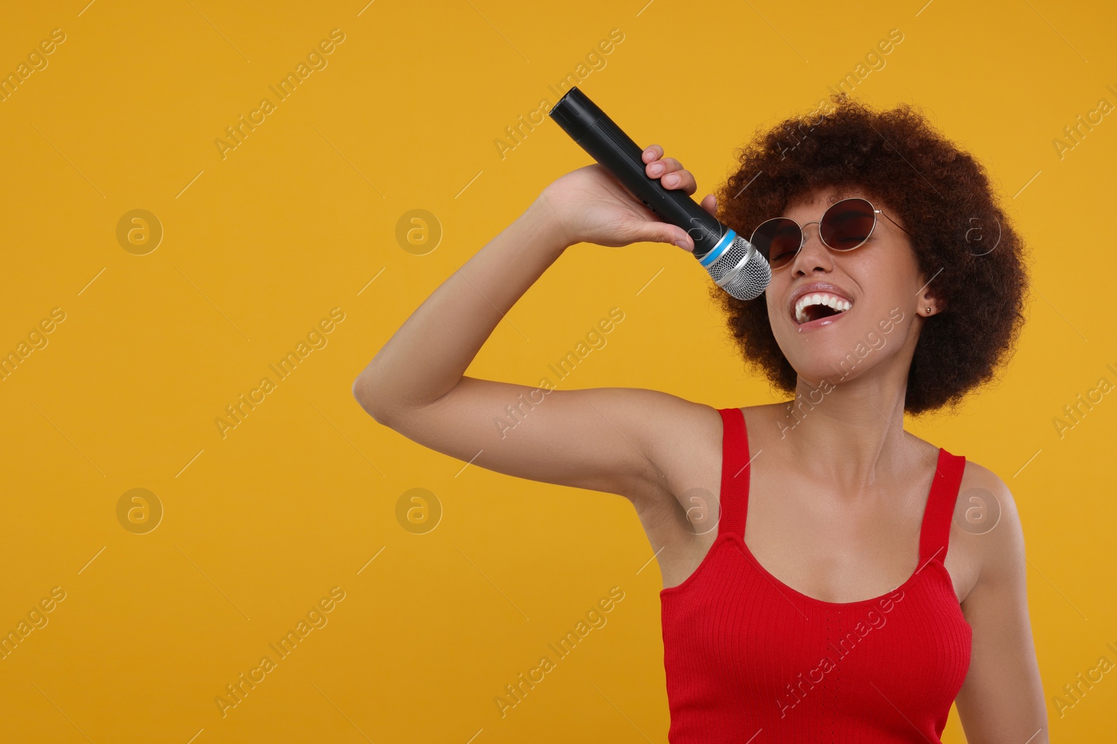 Photo of Curly young woman with microphone singing on yellow background, space for text