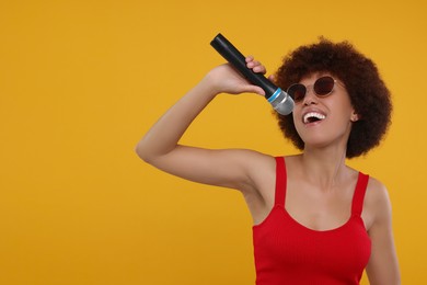Photo of Curly young woman with microphone singing on yellow background, space for text