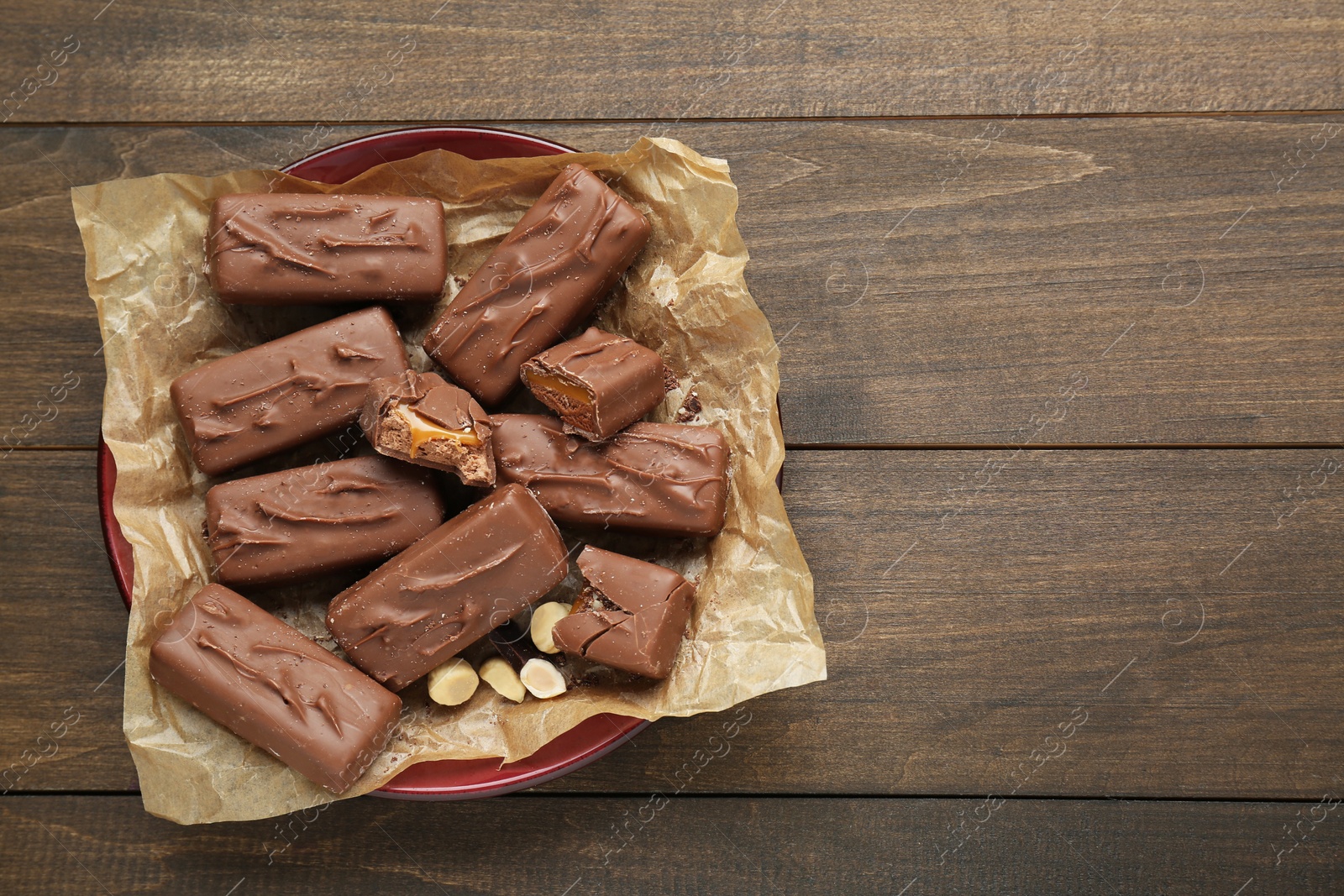 Photo of Many tasty chocolate bars with caramel and nuts on wooden table, top view. Space for text