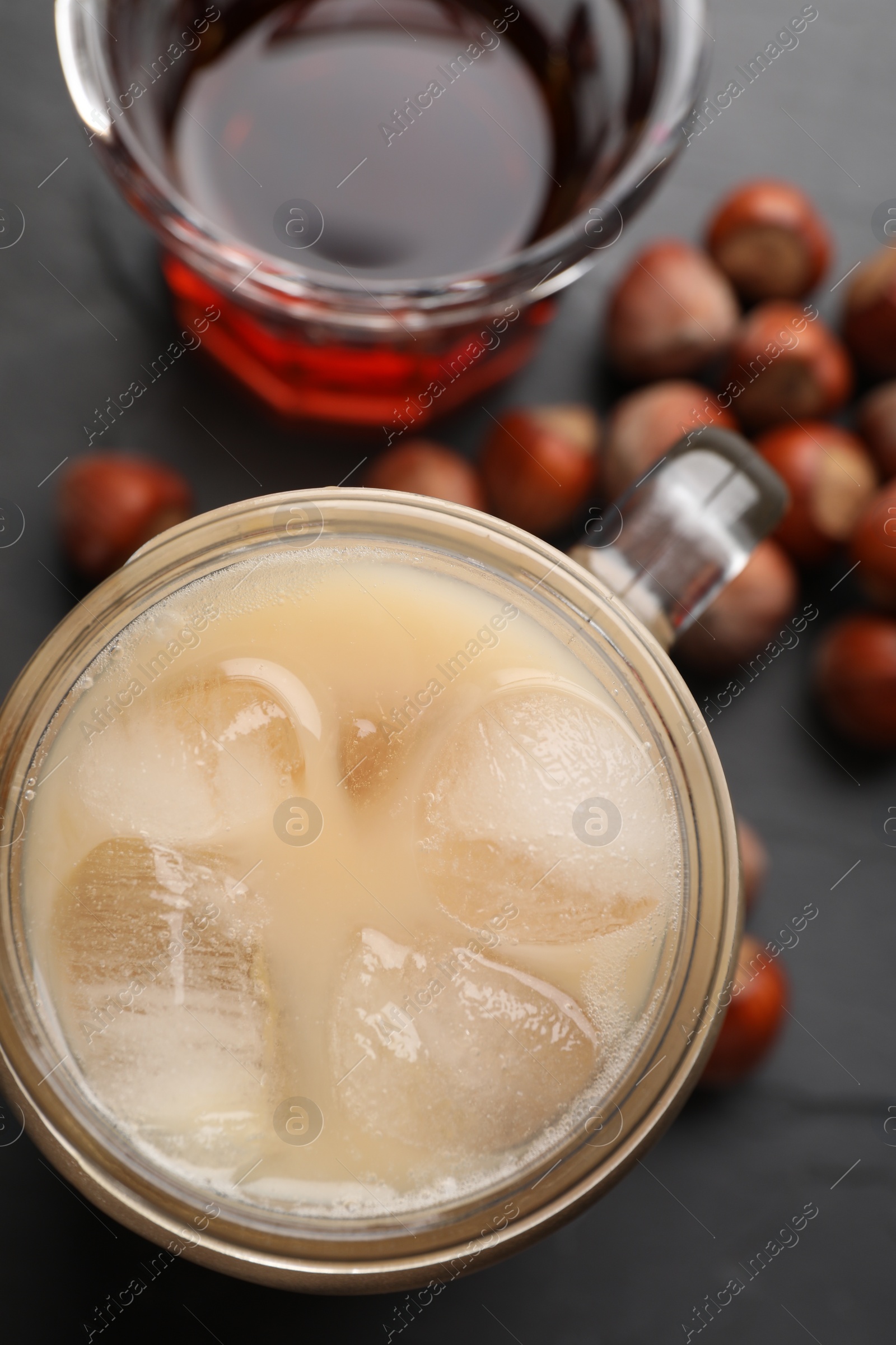 Photo of Mason jar of delicious iced coffee, syrup and hazelnuts on black table, flat lay