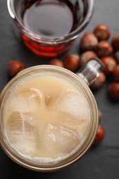 Photo of Mason jar of delicious iced coffee, syrup and hazelnuts on black table, flat lay