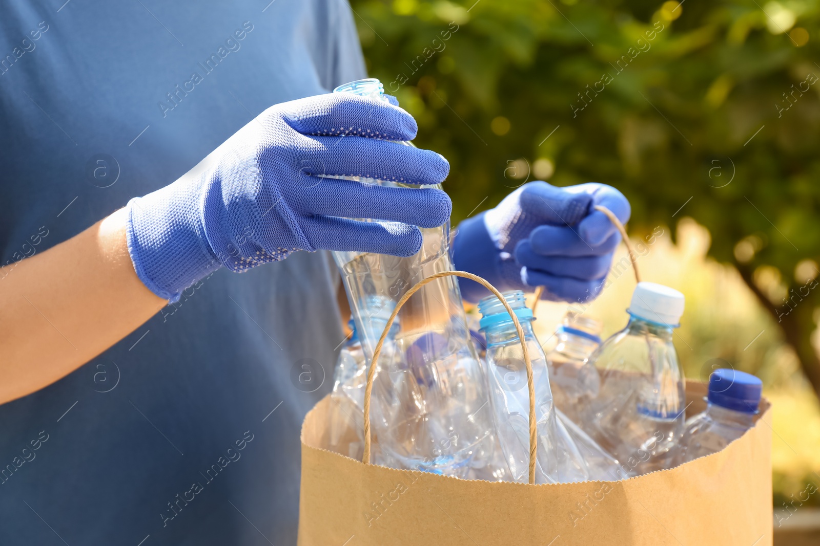 Photo of Woman putting used plastic bottle into paper bag outdoors, closeup. Recycling problem