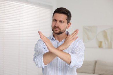 Photo of Handsome man with crossed hands at home. Stop gesture