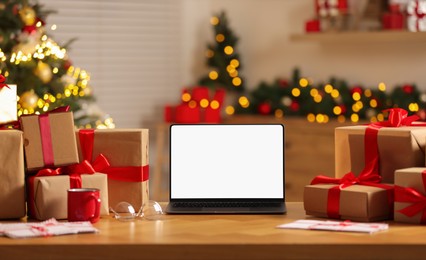 Photo of Christmas time. Laptop with blank screen, gift boxes and letters on table at home