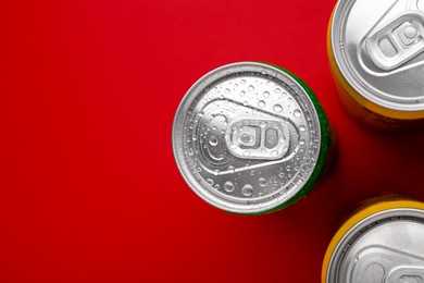 Photo of Energy drinks in wet cans on red background, top view. Space for text