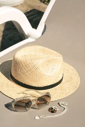 Stylish hat, sunglasses and jewelry on grey sunbed outdoors