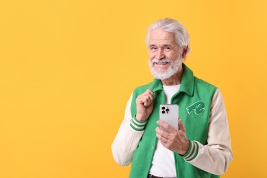 Photo of Portrait of stylish grandpa using smartphone on yellow background, space for text