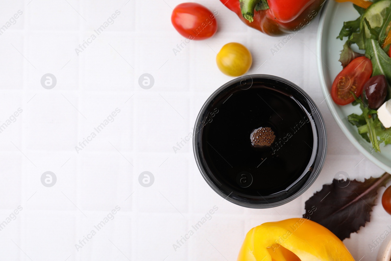 Photo of Vinegar in glass, salad and products on white tiled table, flat lay. Space for text