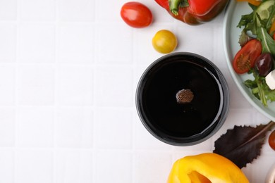 Vinegar in glass, salad and products on white tiled table, flat lay. Space for text