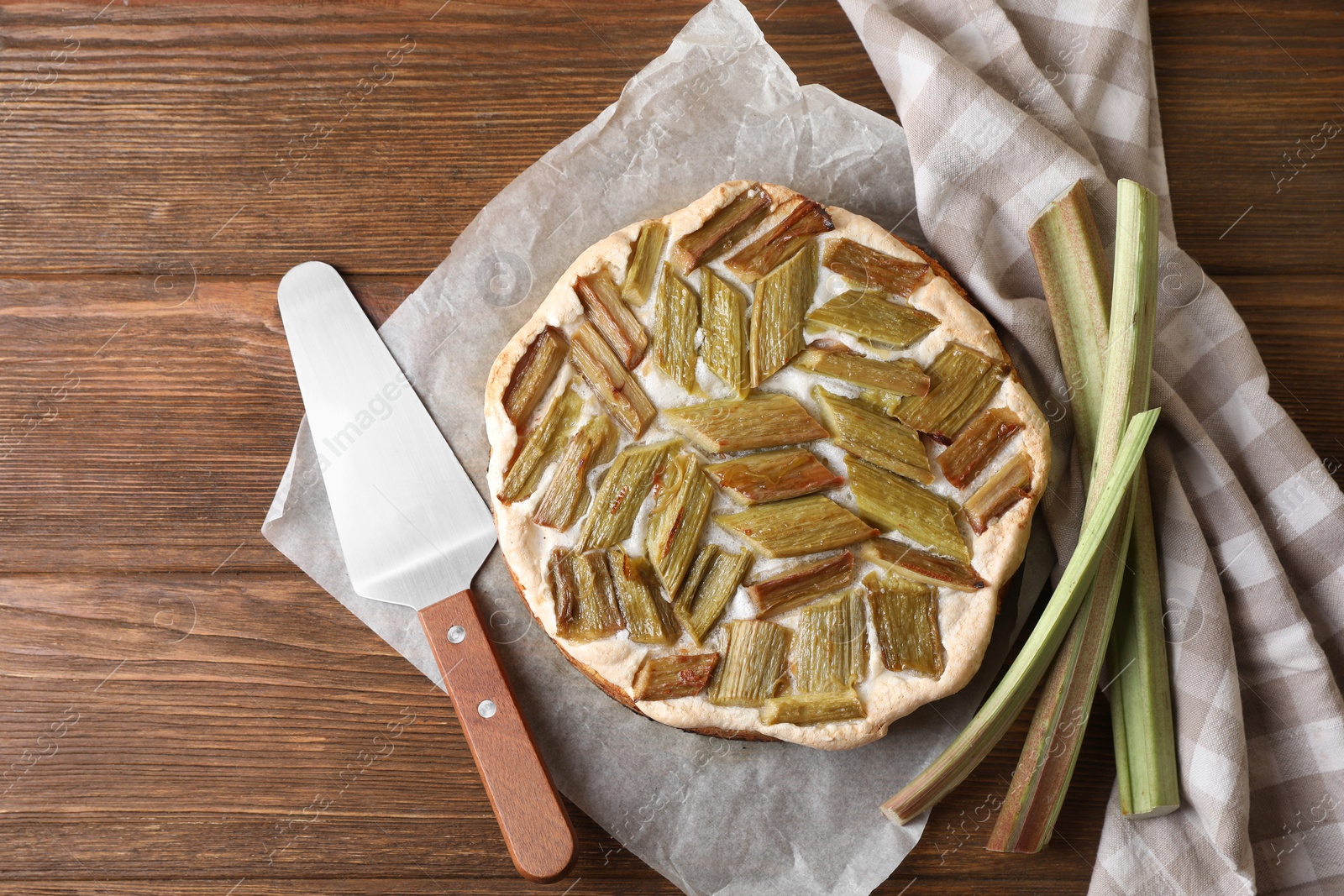 Photo of Freshly baked rhubarb pie, stalks and spatula on wooden table, flat lay. Space for text