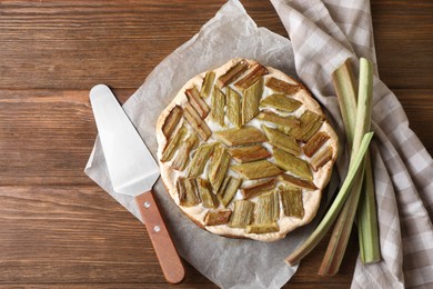 Freshly baked rhubarb pie, stalks and spatula on wooden table, flat lay. Space for text
