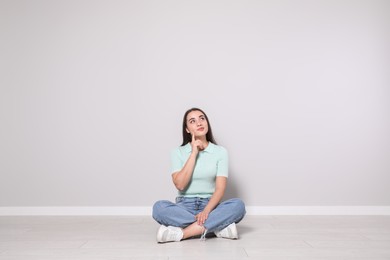 Young woman sitting on floor near light grey wall indoors