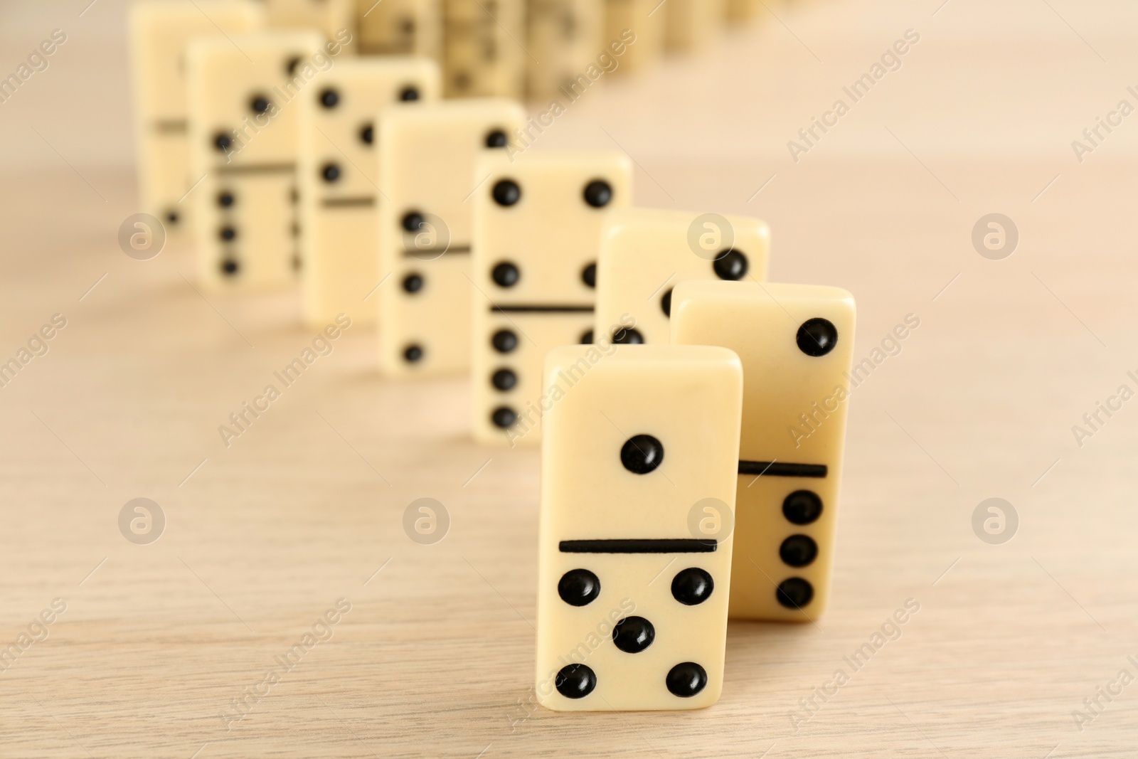 Photo of White domino tiles with black pips on wooden table, closeup