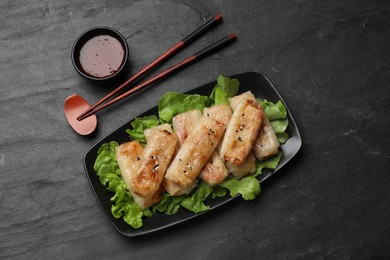 Photo of Tasty fried spring rolls, lettuce and sauce on black table, top view