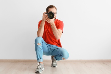 Young photographer with professional camera near white wall