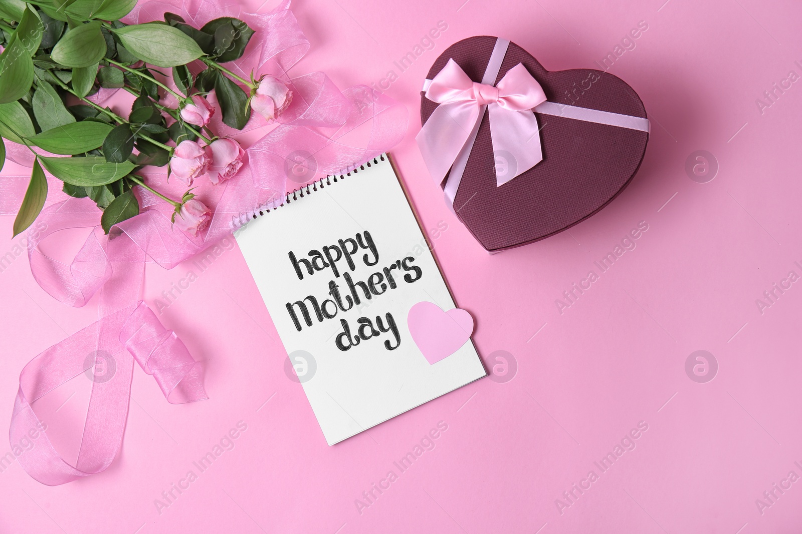 Photo of Notebook with phrase "HAPPY MOTHER'S DAY", flowers and gift box on color background