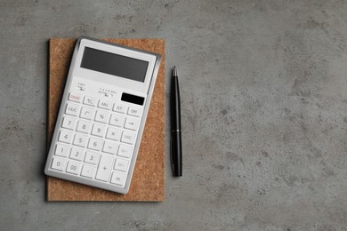 Calculator, notebook and pen on grey table, flat lay with space for text