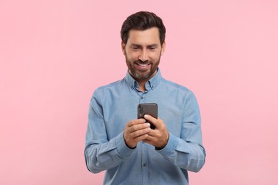 Photo of Handsome bearded man using smartphone on pink background