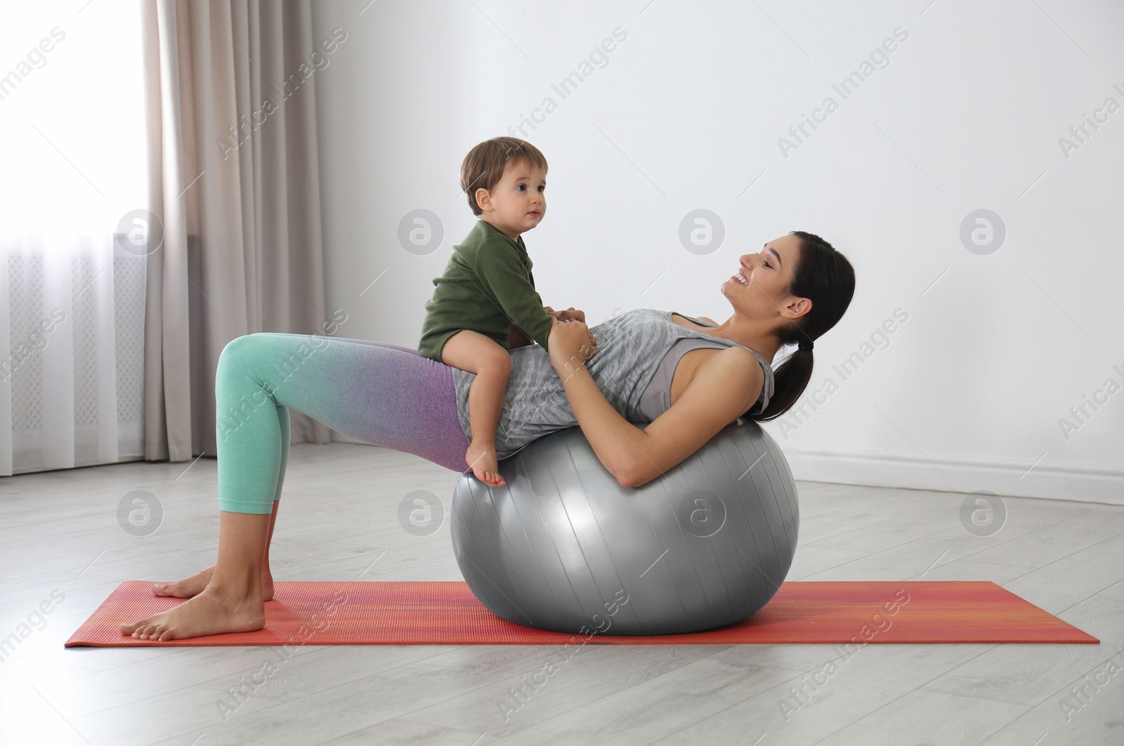 Photo of Young woman doing exercise with her son indoors. Home fitness