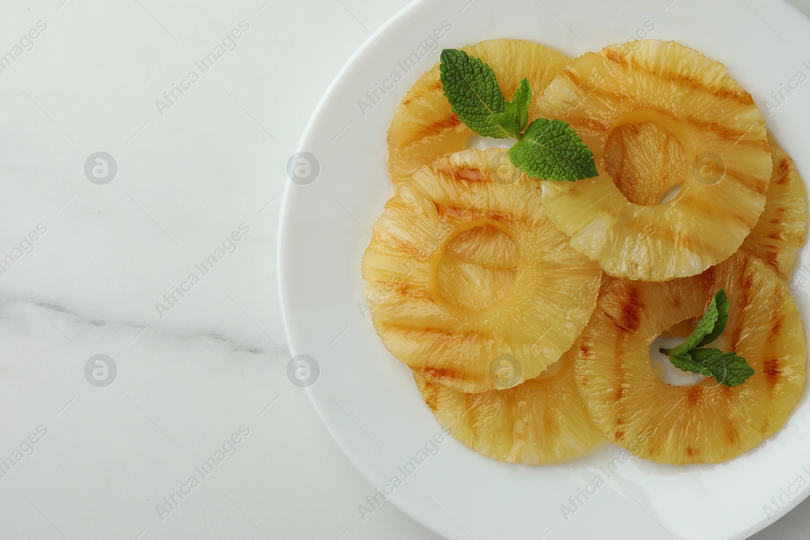 Photo of Tasty grilled pineapple slices with mint on white table, top view. Space for text