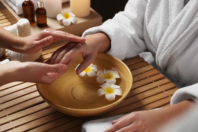 Woman receiving hand massage in spa salon, closeup. Bowl of water and flowers on wooden table