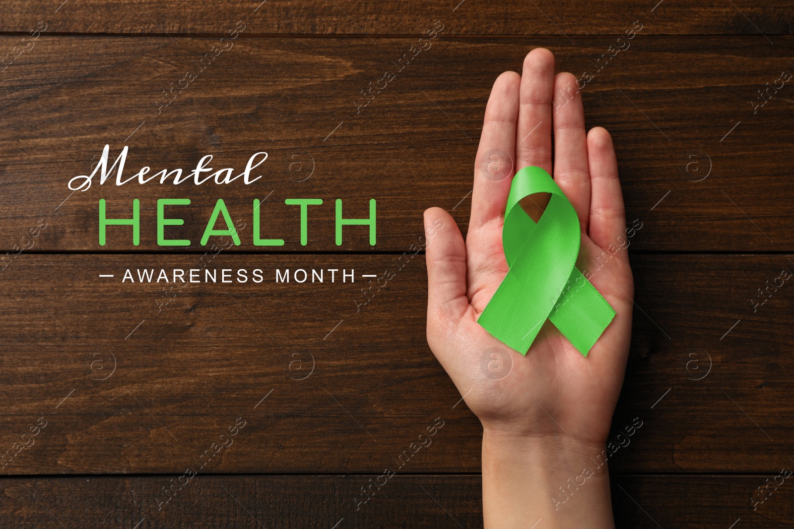 Image of World Mental Health Day. Woman holding green ribbon at wooden table, top view