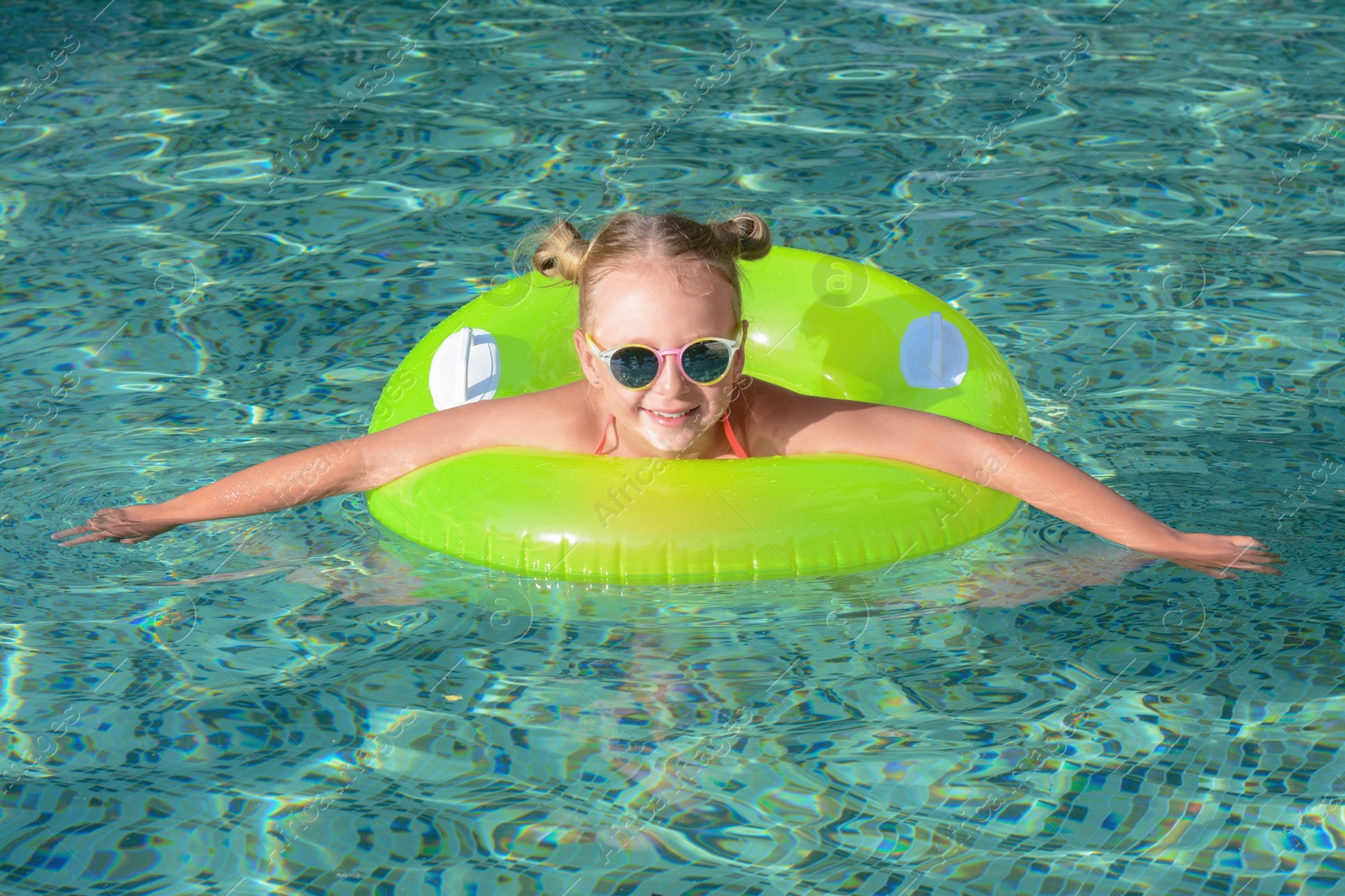 Photo of Happy little girl with inflatable ring in outdoor swimming pool on sunny day