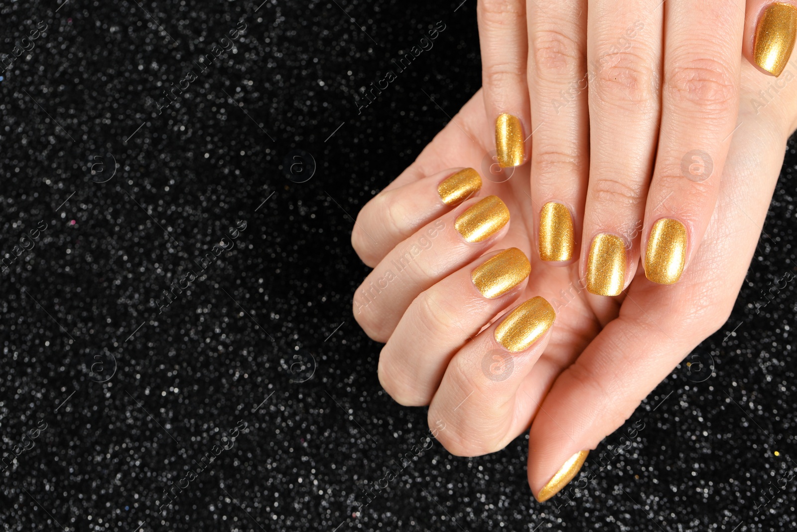 Photo of Woman showing manicured hands with golden nail polish on black background, closeup. Space for text