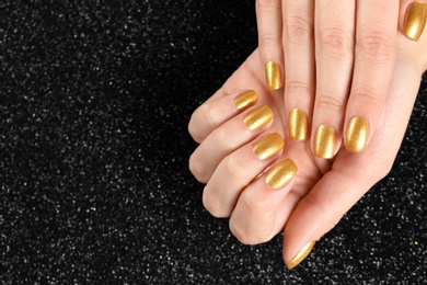 Photo of Woman showing manicured hands with golden nail polish on black background, closeup. Space for text